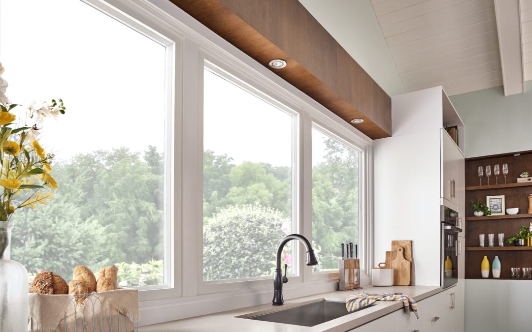 A clean white kitchen with three large windows behind a single-basin kitchen sink.