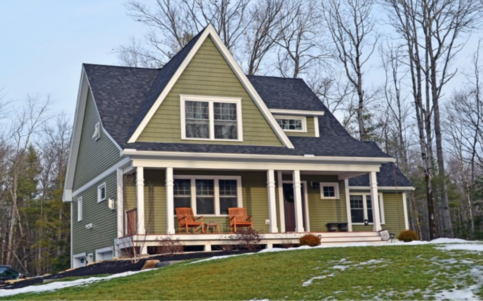  et hus med grøn sidespor og hvid trim sidder på toppen af en snedækket bakke.