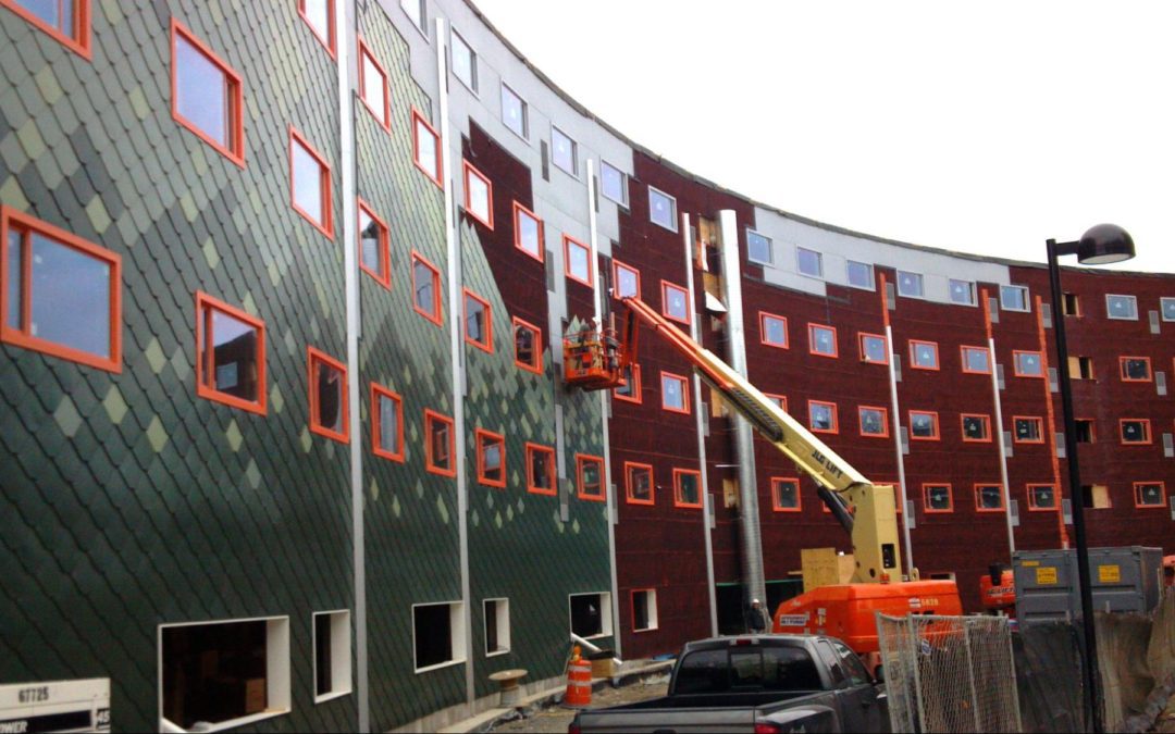 A side view of a commercial building as green cladding is installed, complementing the orange-framed Paradigm windows.