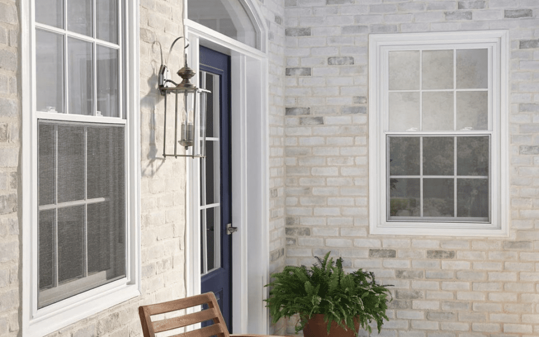 White and grey toned brick home exterior with a dark blue door, two windows and outdoor chairs.