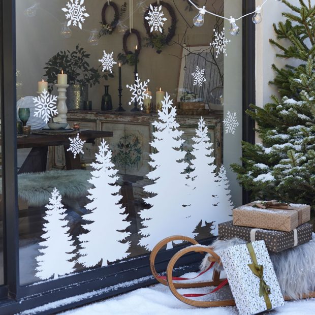 This window features white tree and snowflake stickers, and there is a winter display in front of the window including a sleigh, presents and a pine tree.