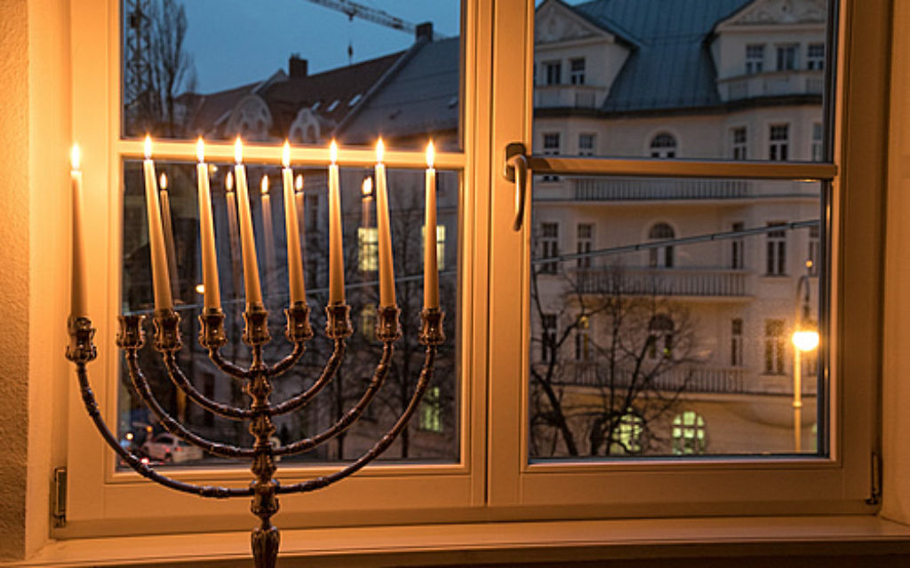 This window has a menorah with eight lit candles giving off a warm hue, overlooking a view of neighboring homes.